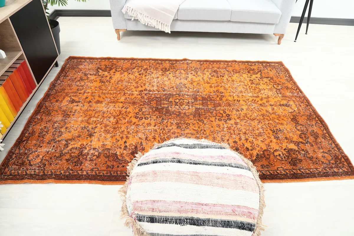 Full overhead view of the orange vintage rug in a styled room, centered with an ottoman.