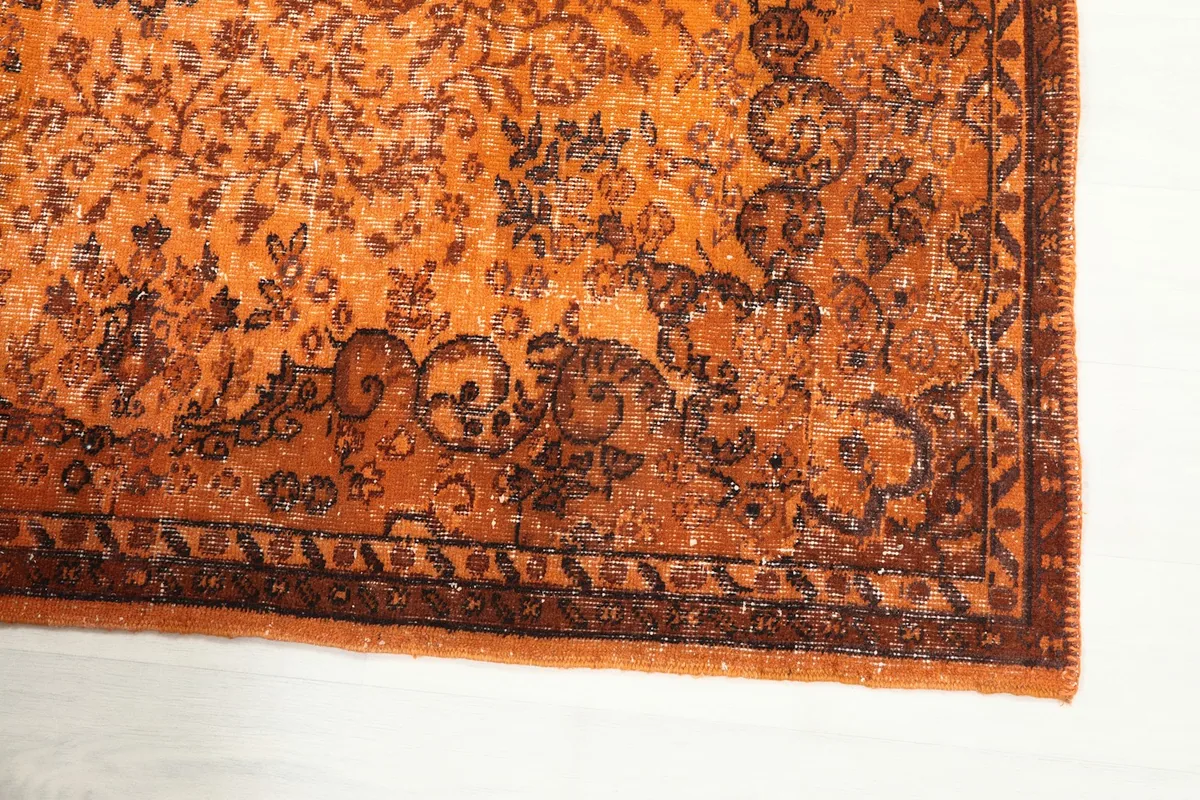 Detailed view of the rug's brown border and corner, highlighting the intricate faded motifs.