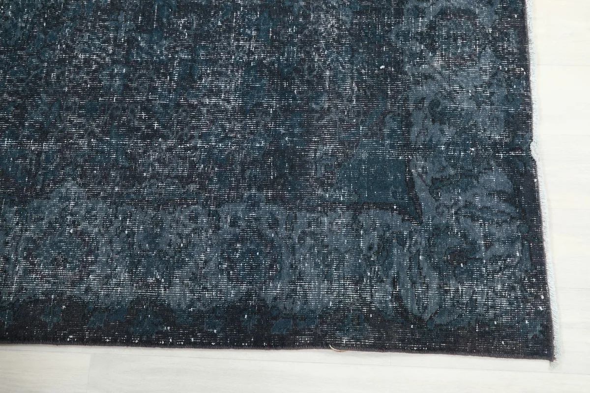 Corner detail of the navy rug, showing the faded border and the subtle texture of the low pile.