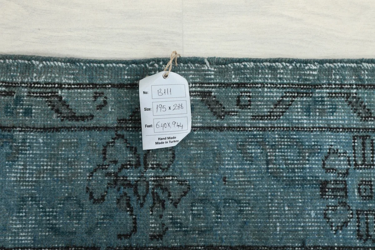 Tag showing the rug's dimensions and origin, attached to the edge of the blue vintage rug