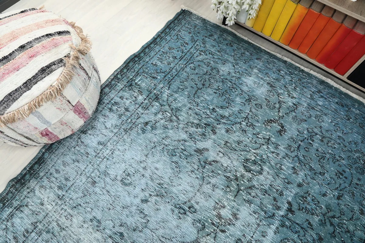 Corner view of the rug next to an ottoman, emphasizing the blue color and distressed look.