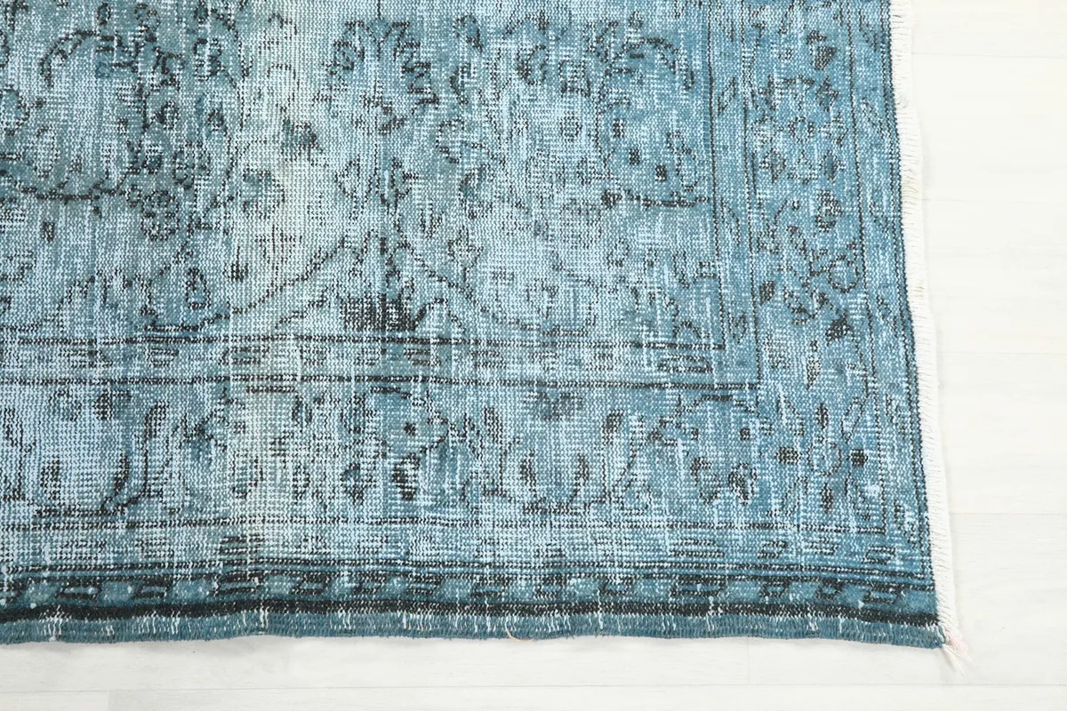 Detail of the rug's border, showcasing the faded blue and charcoal geometric motifs.
