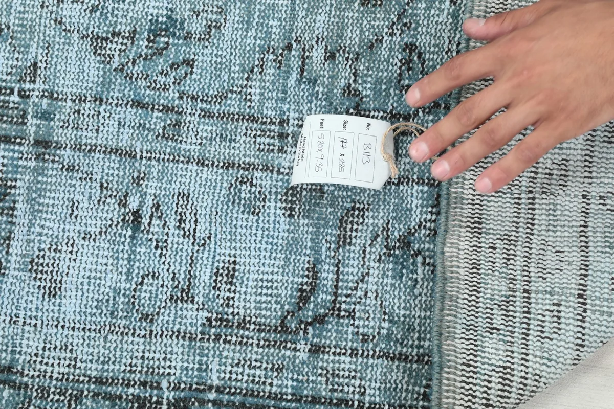 Hand pointing to the tag on the back of the rug, displaying product information and origin.