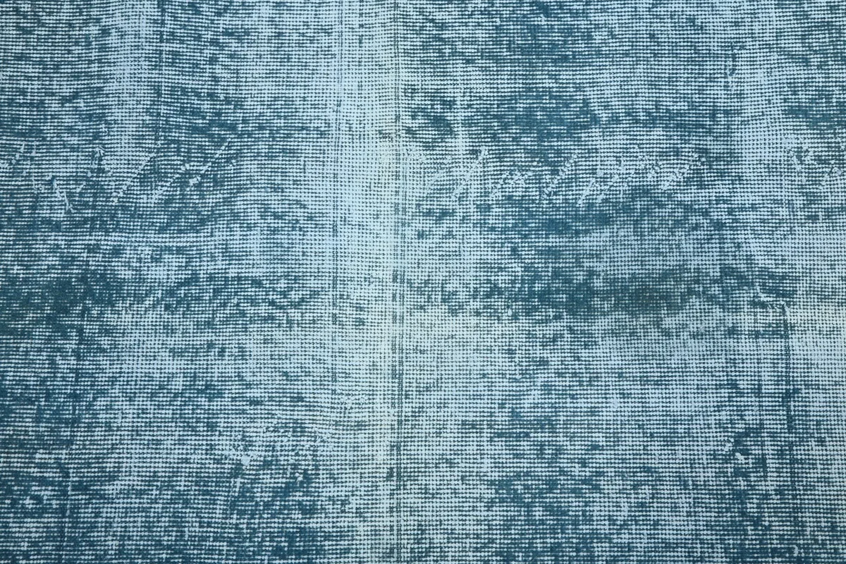 Overhead detail of the rug's texture, showing the faded design and hand-knotted wool pile.