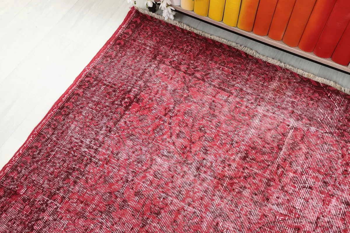 Corner view of the rug, showing the blend of rose and faded red tones and the low pile.