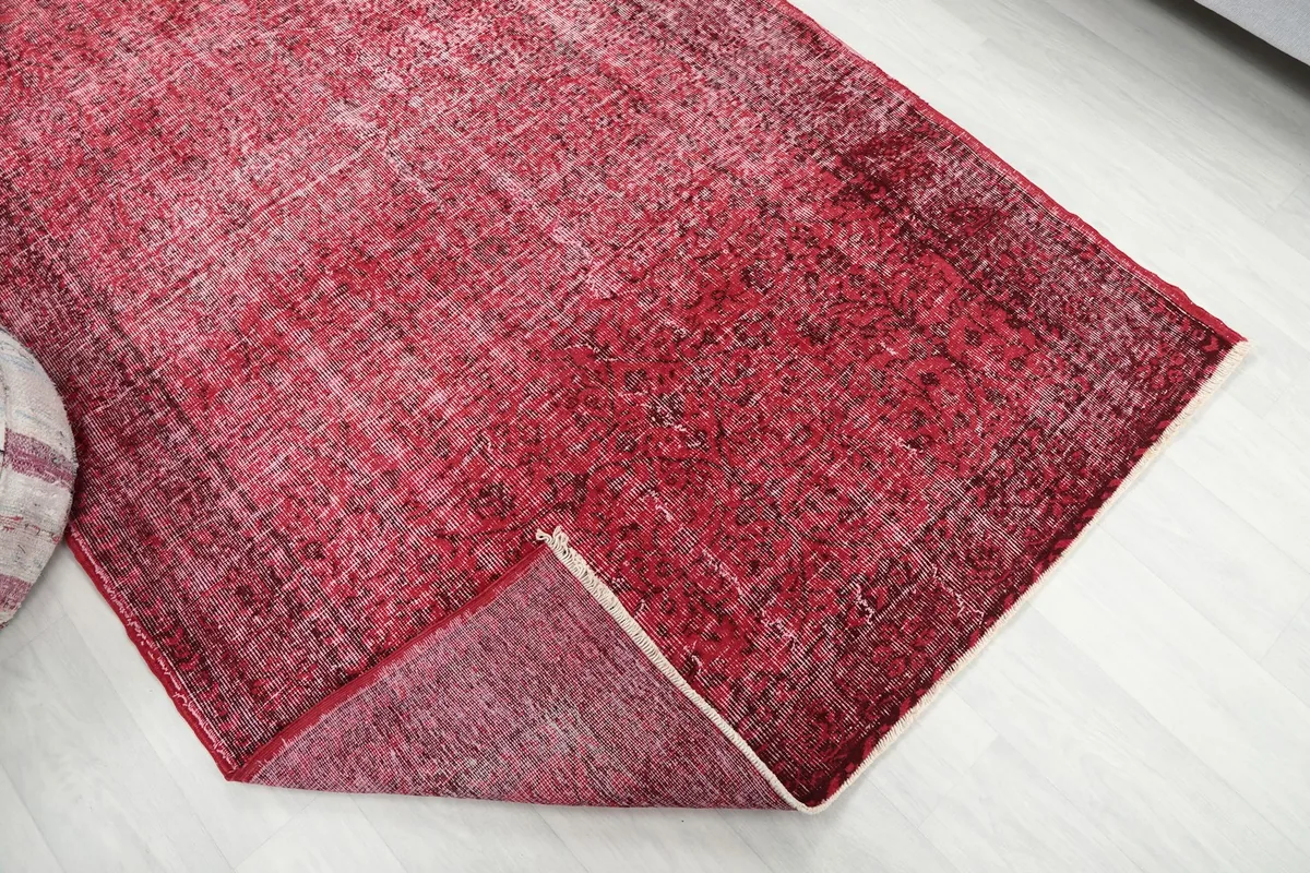 The corner of the rose rug folded back, showing the back of the hand-knotted cotton foundation.