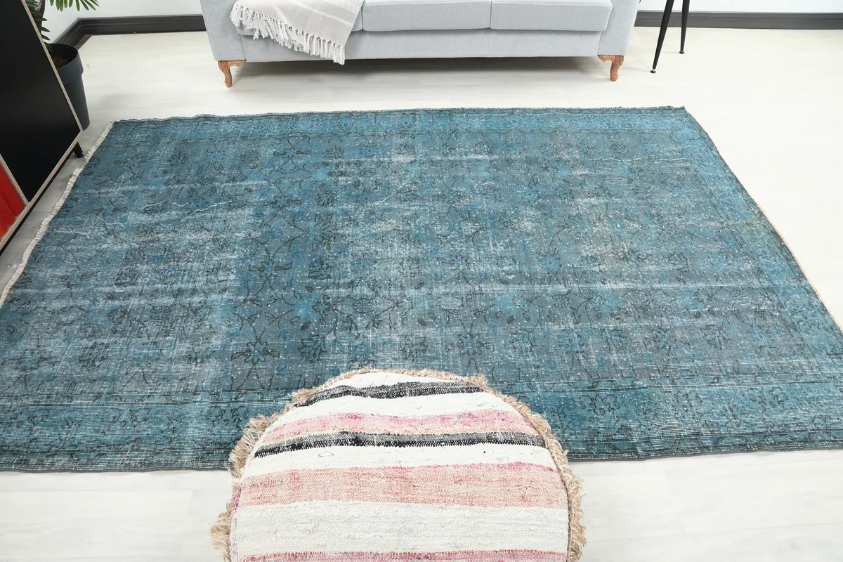 Full view of the Blue Gray Faded Floral Anatolian Rug centered in a room, with an ottoman for scale.
