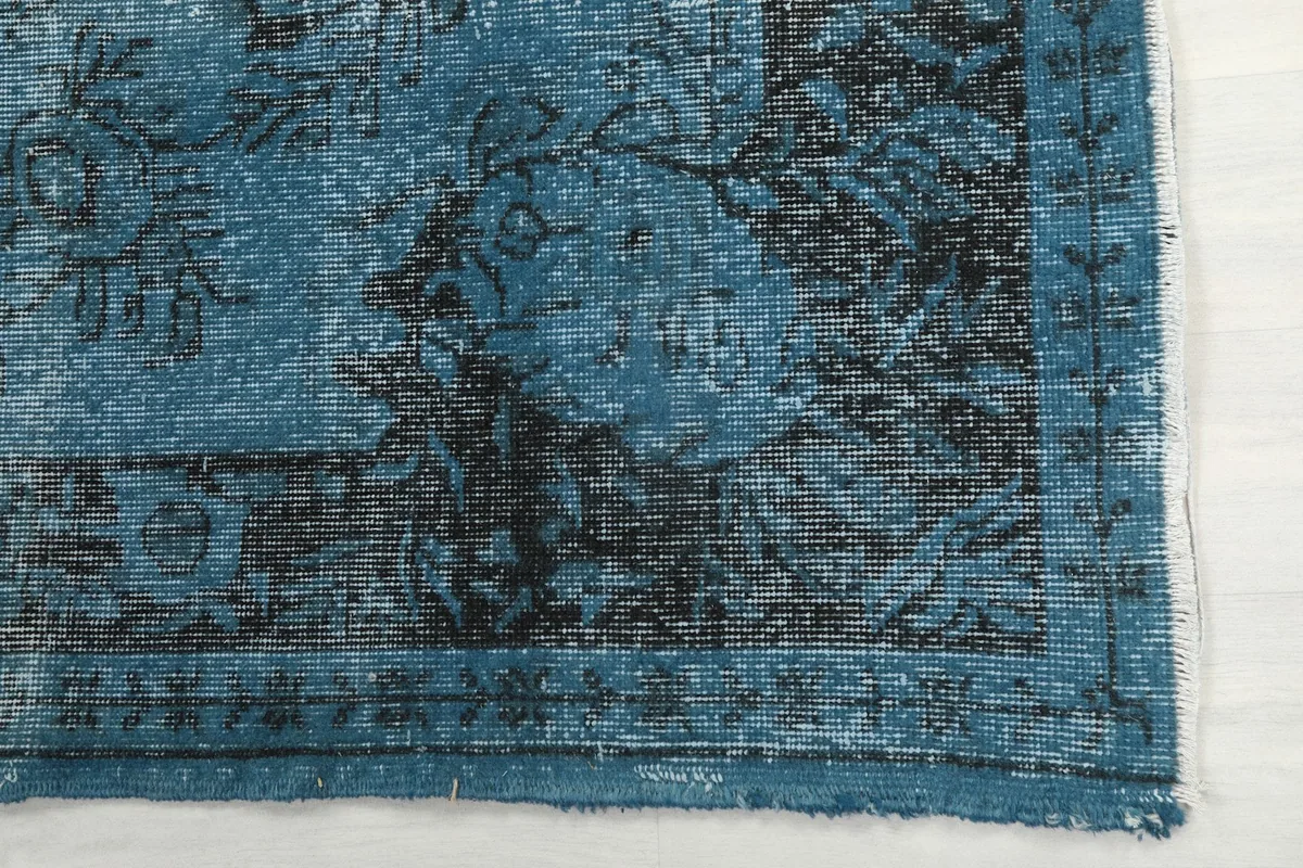 Detail of the rug's corner, showing the blue and charcoal floral border pattern and low pile