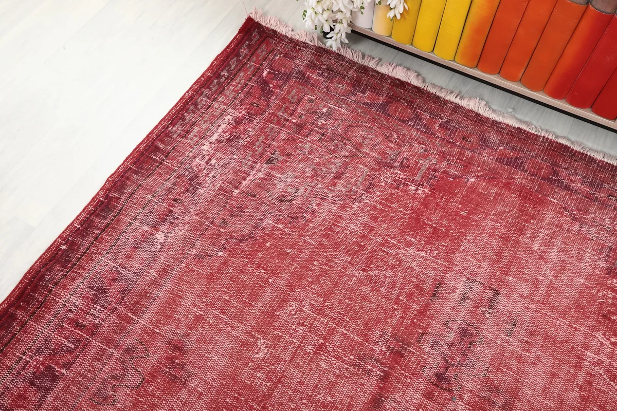 Corner view of the red vintage rug, showing the distressed pattern and the short, light fringes