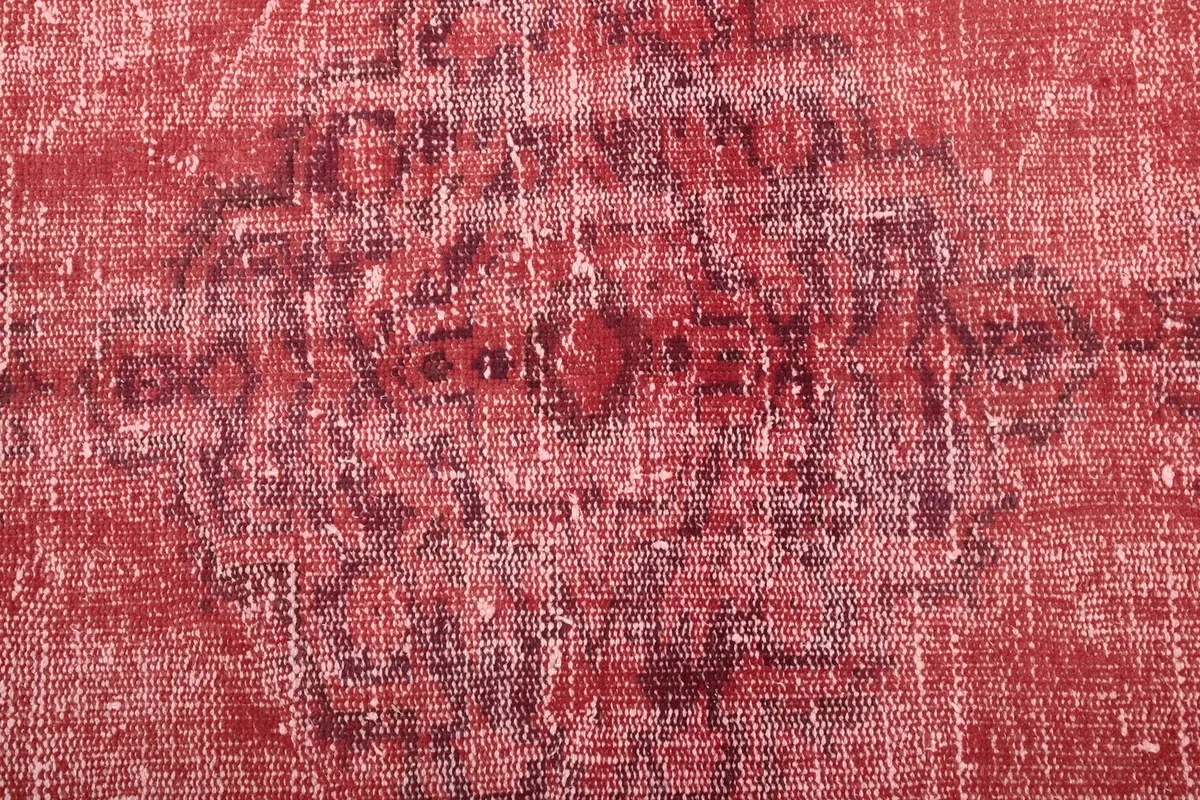 Very close detail of the rug's surface, highlighting the faded red and ivory colors and wool texture