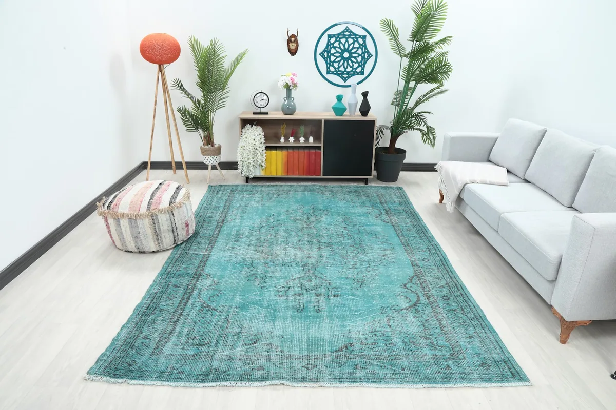Blue and charcoal vintage Anatolian rug displayed in a bright living room setting with a sofa and plants.