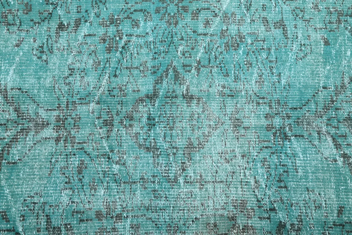 Close-up of the rug's low pile, revealing the hand-knotted wool texture and faded charcoal patterns on blue.
