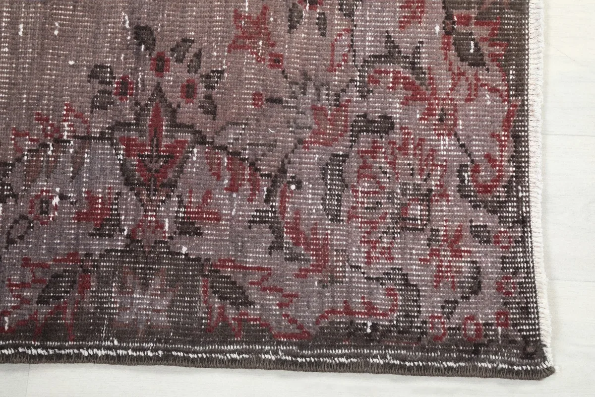 Detailed view of the corner of the rug, showing the faded rose and brown motifs and low pile