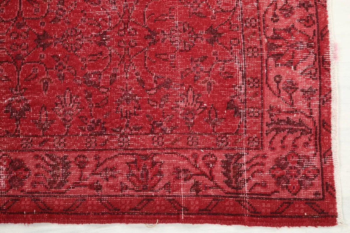 Detailed view of the corner of the red rug, showing the border design and color variations.