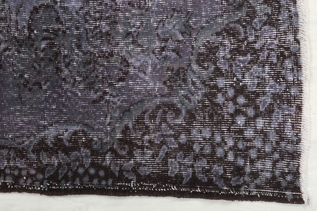 Close-up detail of the charcoal border and faded purple field of the rug