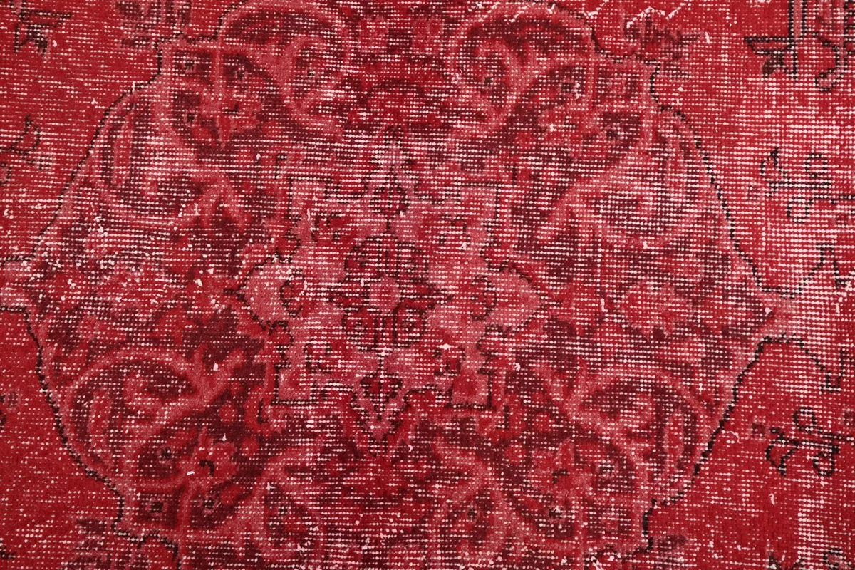 Close-up of the faded floral and geometric motifs within the red pile.