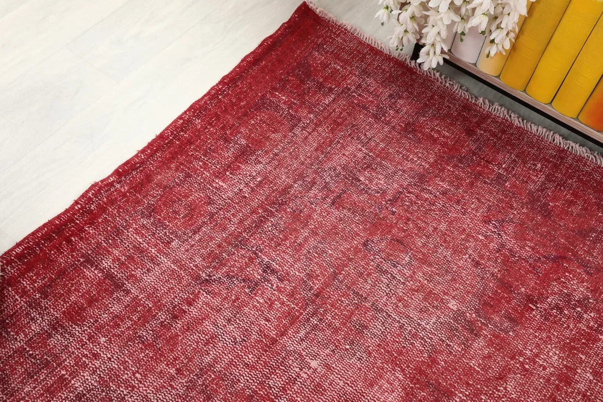 Corner view of the red distressed vintage rug, showing the faded red tones and wool texture.