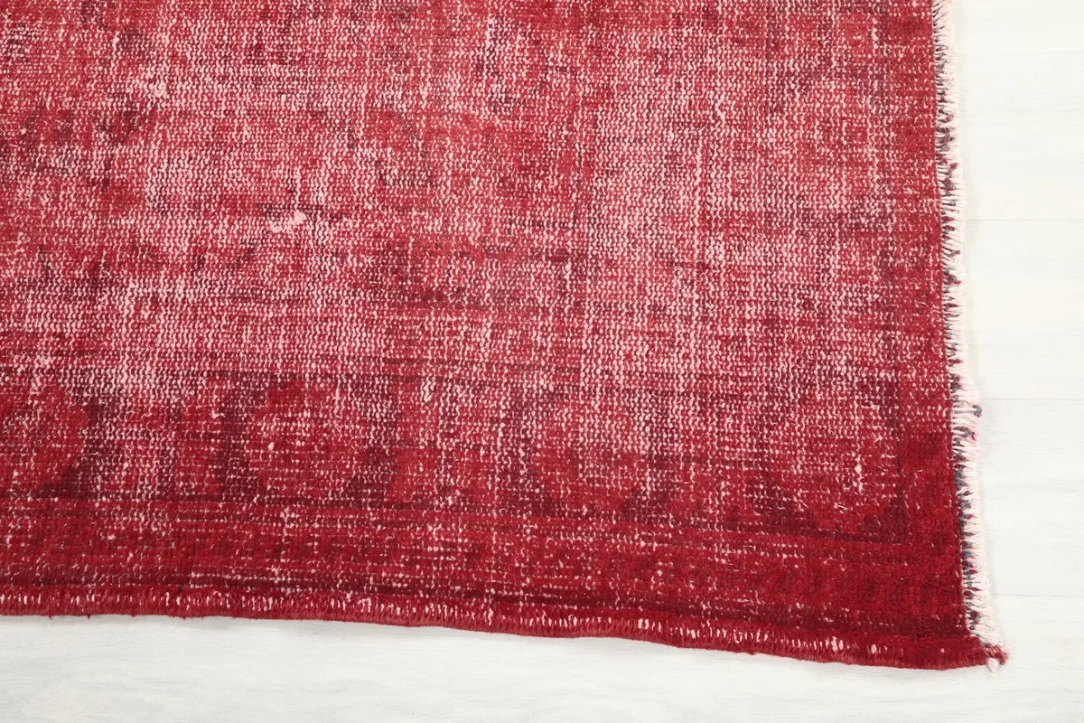 Detailed view of the rug's edge, showcasing the distressed red pile and subtle fringed finish.