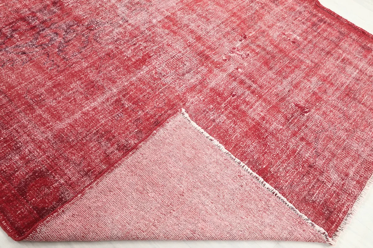Corner of the red vintage rug folded back to reveal the cotton foundation and hand-knotted construction.