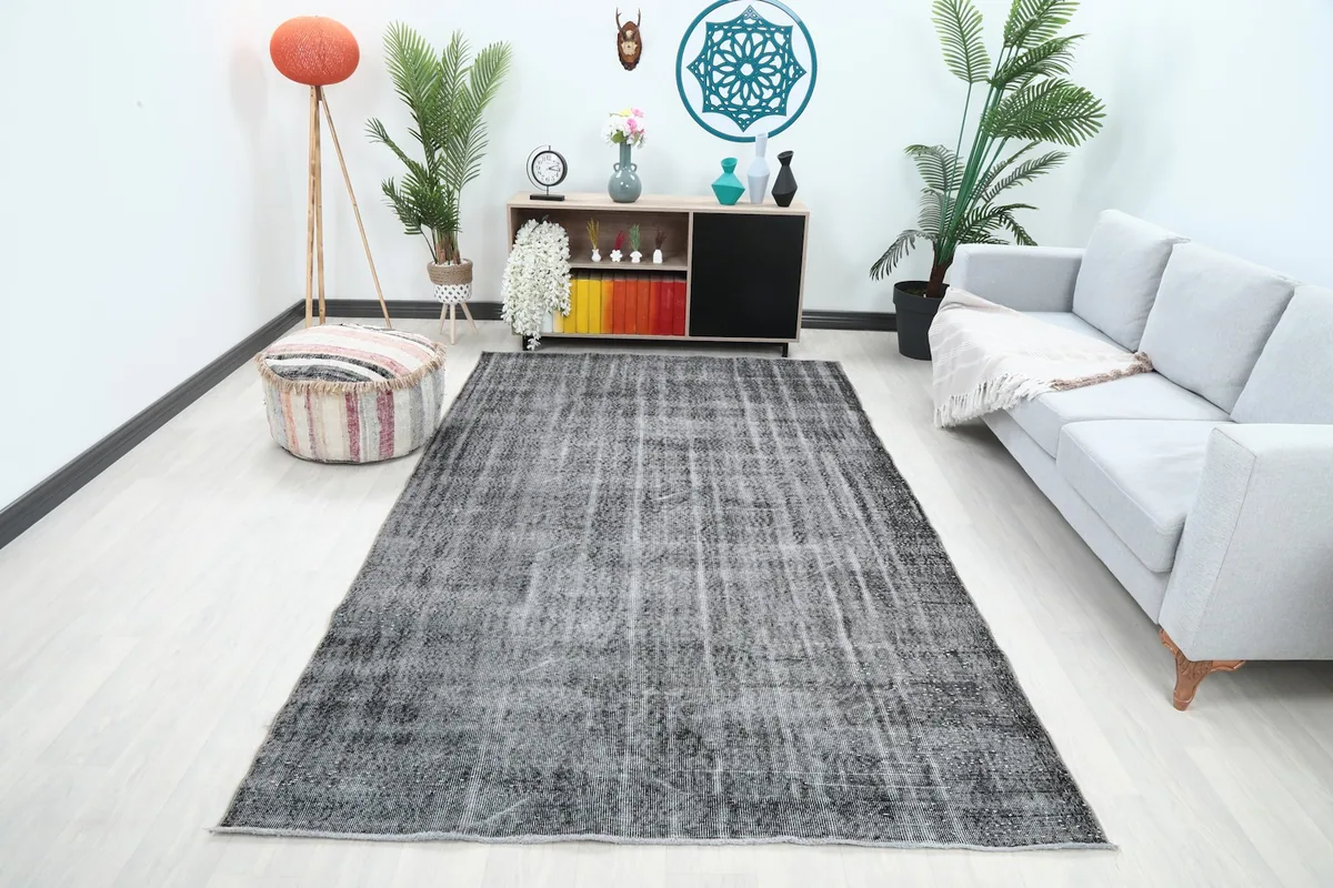 Vintage charcoal rug displayed in a bright living room setup with a gray sofa and plants.