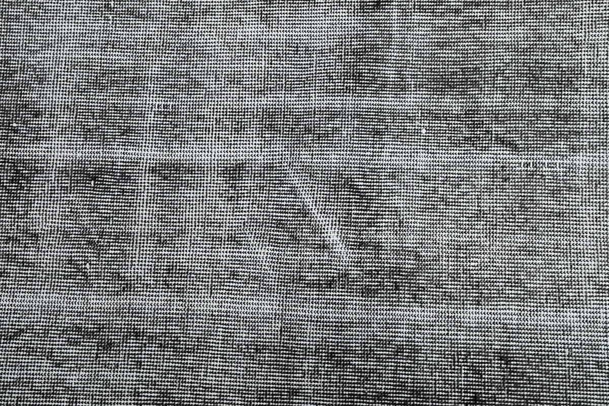 Overhead detail of the rug's faded pattern, revealing hints of original design under the charcoal wash.