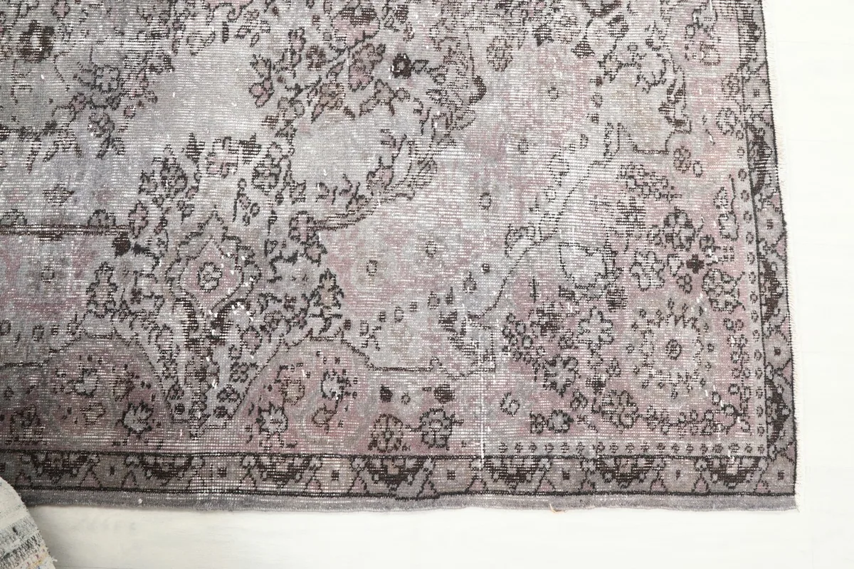 Detailed view of the rug's border and corner, highlighting the charcoal geometric motifs and rose tones.