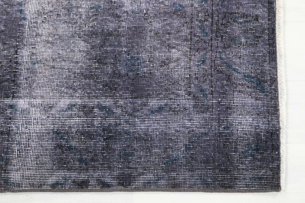 Detailed view of the rug's distressed surface, showing faded charcoal and hints of blue.