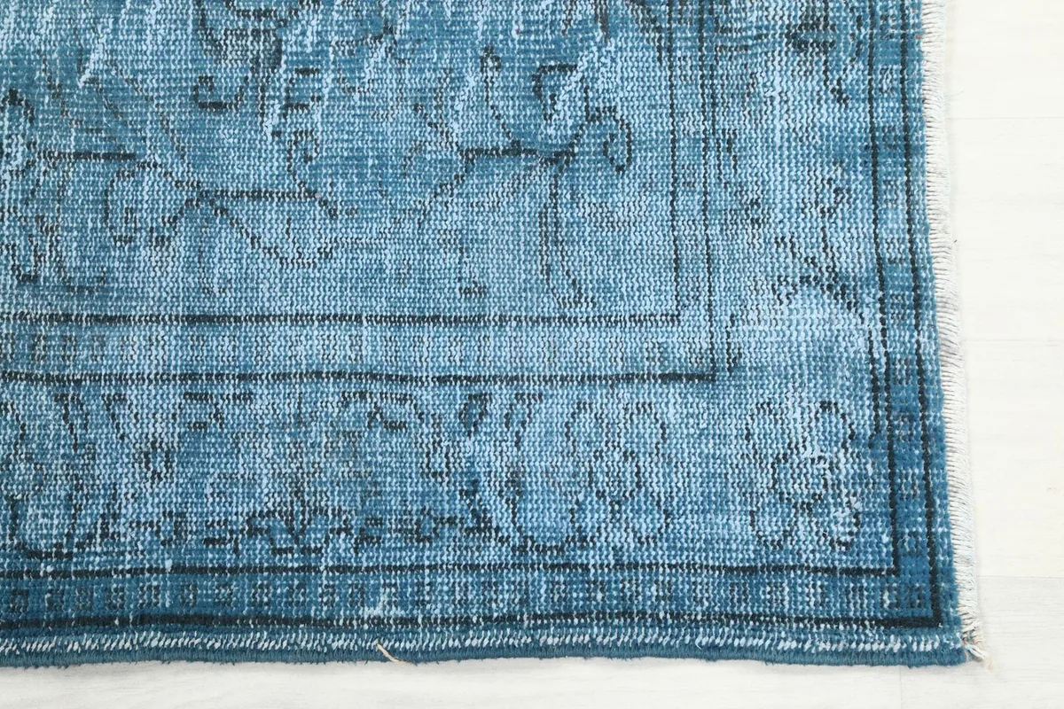 Close-up of the distressed blue border and faded floral motifs of the hand-knotted rug