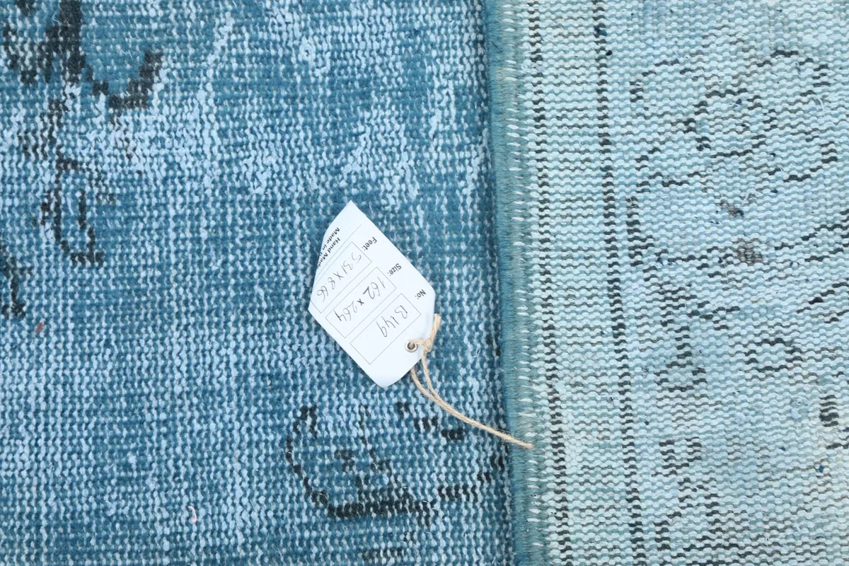 Detail showing the rug's tag alongside the hand-knotted wool pile and cotton foundation