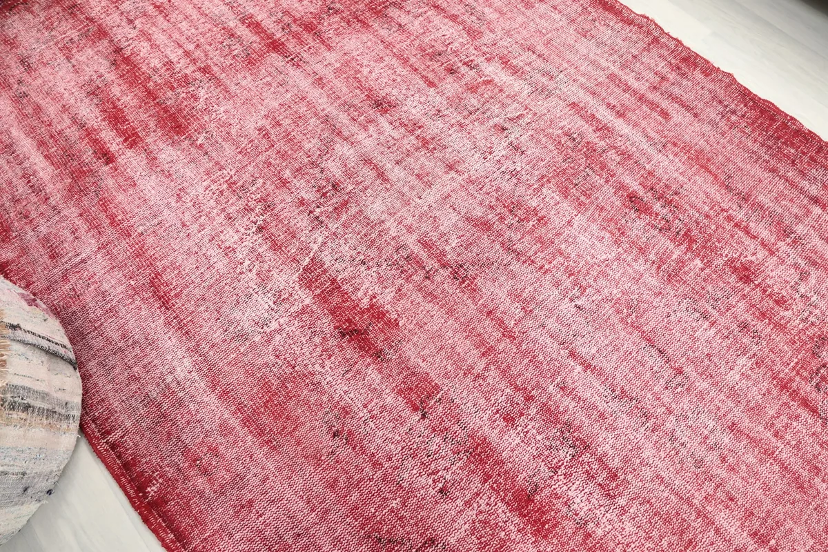 Angled view across the red vintage rug's surface, emphasizing the overall distressed pattern and color variation.