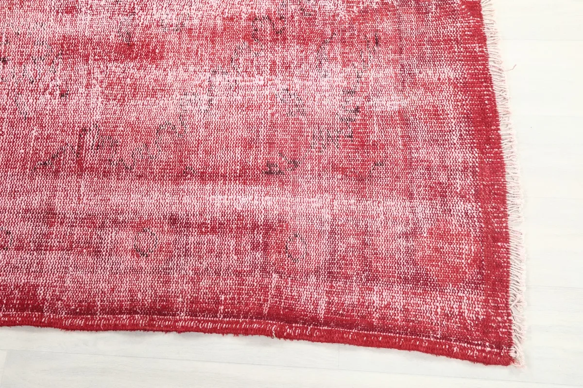 Detail view of the rug's edge, showing the distressed red color and the subtle fringed finish.