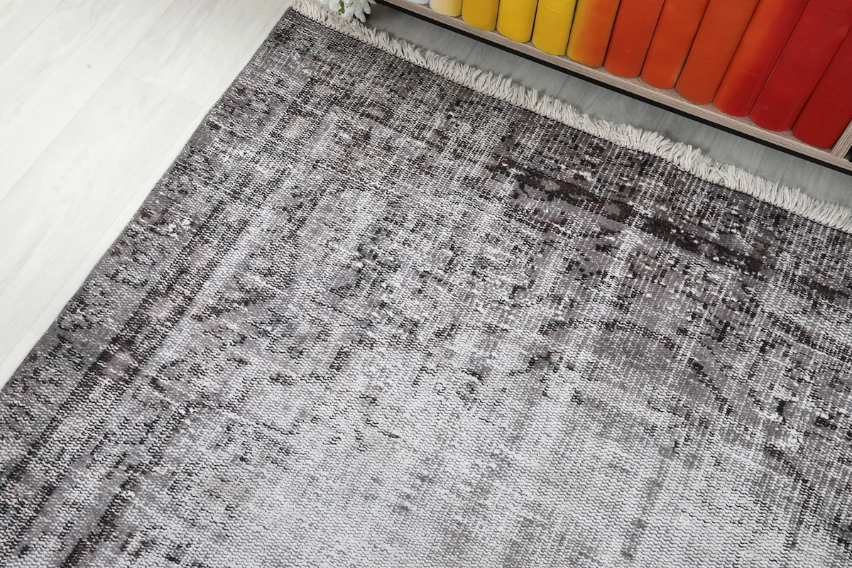 Corner view of the rug, showcasing the charcoal border and ivory central area with distressed details.