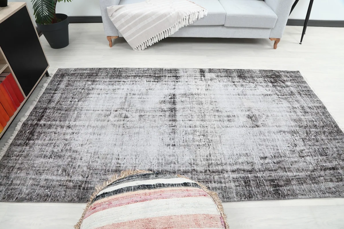 Full room view of the charcoal and ivory vintage rug, showing its scale relative to a sofa and ottoman.