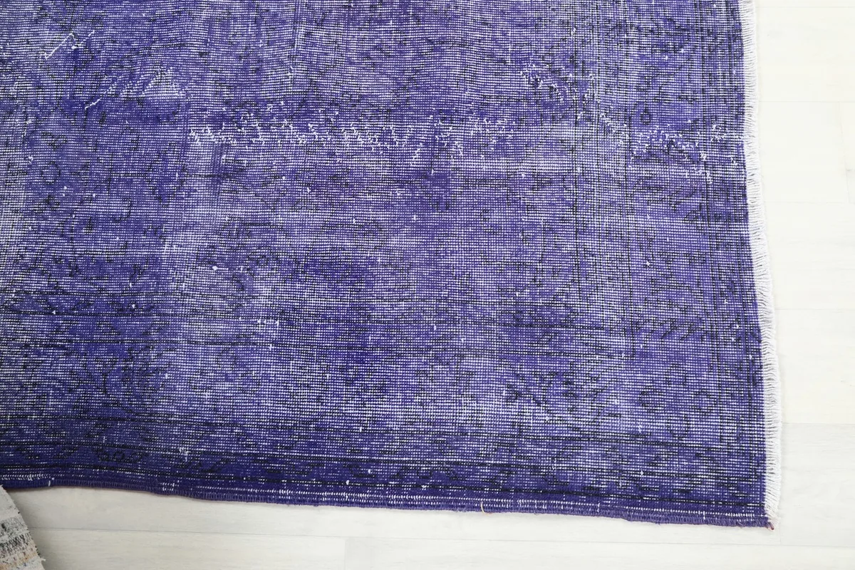 Detailed view of one end of the purple rug, highlighting the faded pile and color variations.
