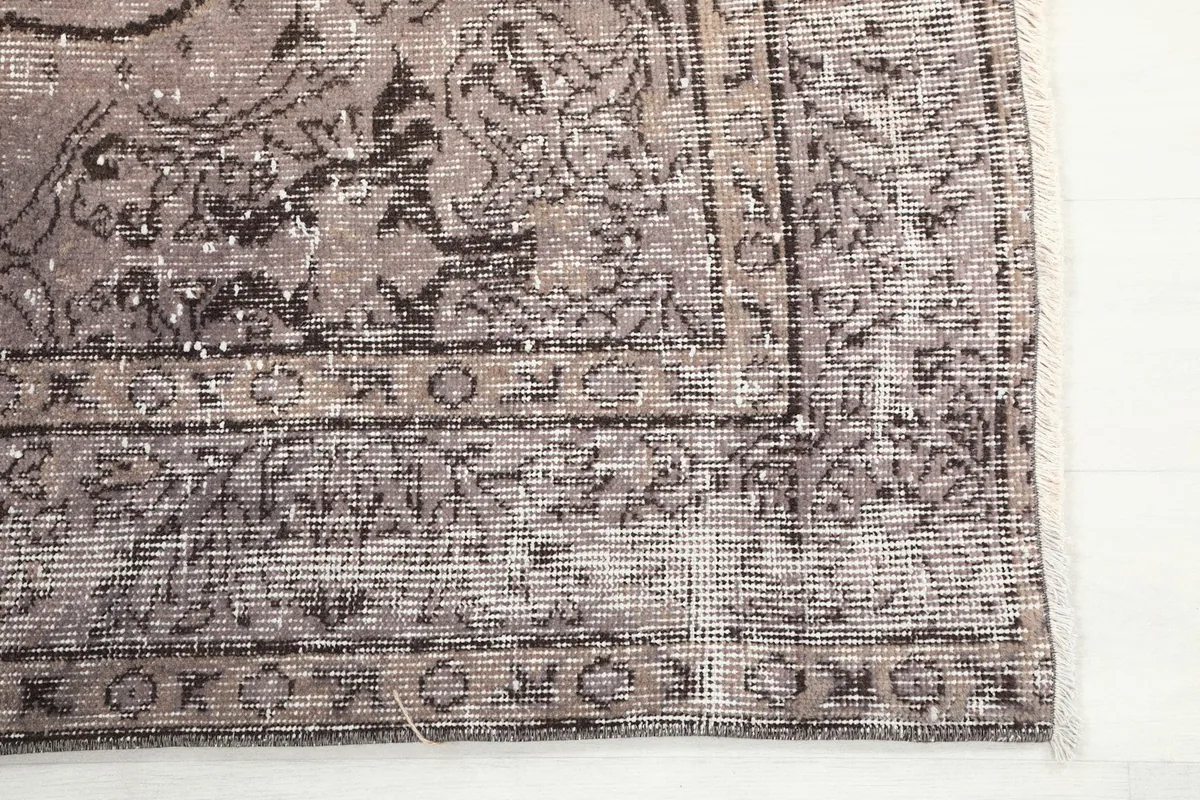 Detailed view of the corner and border of the vintage charcoal gray rug, highlighting the faded design.