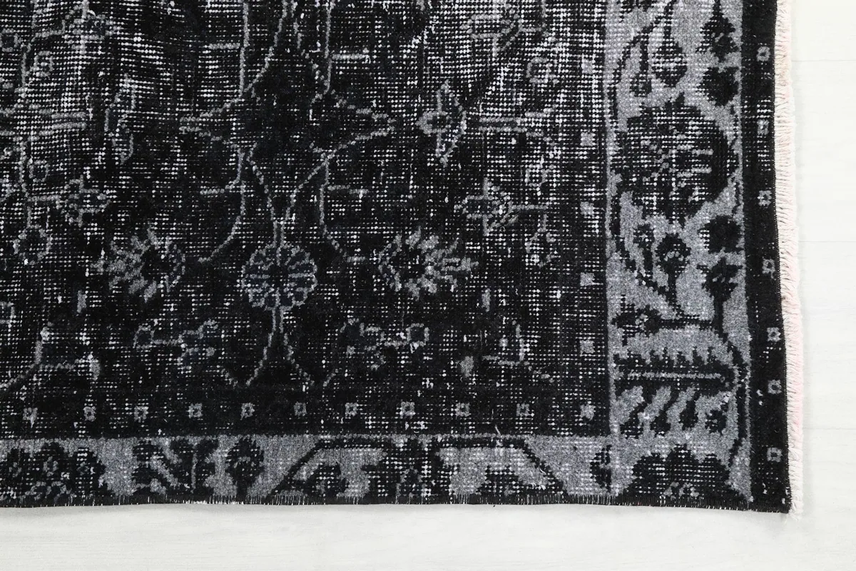 Detailed view of the rug's faded gray floral motifs against the black field and border
