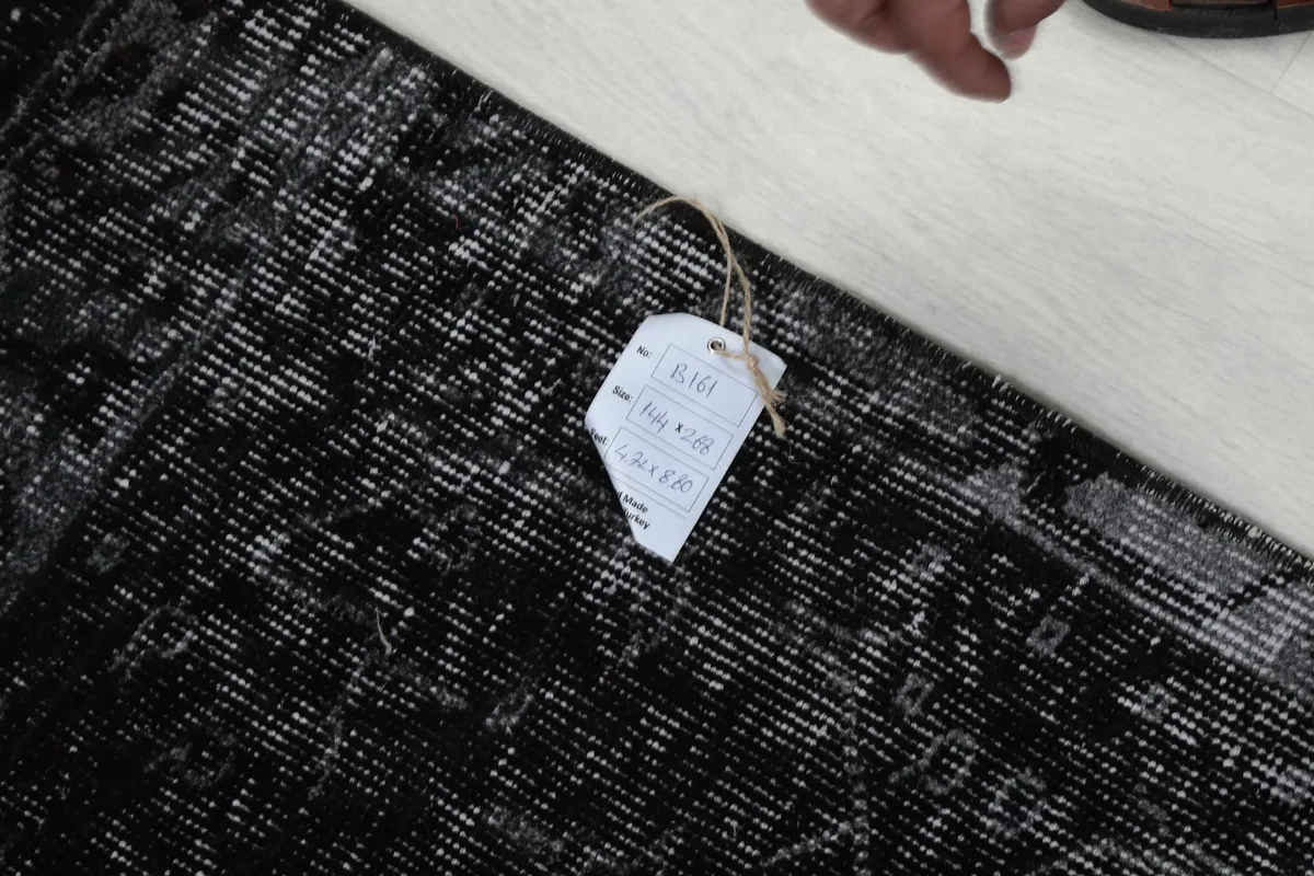 Hand pointing to the tag on the rug, indicating its size and vintage authenticity