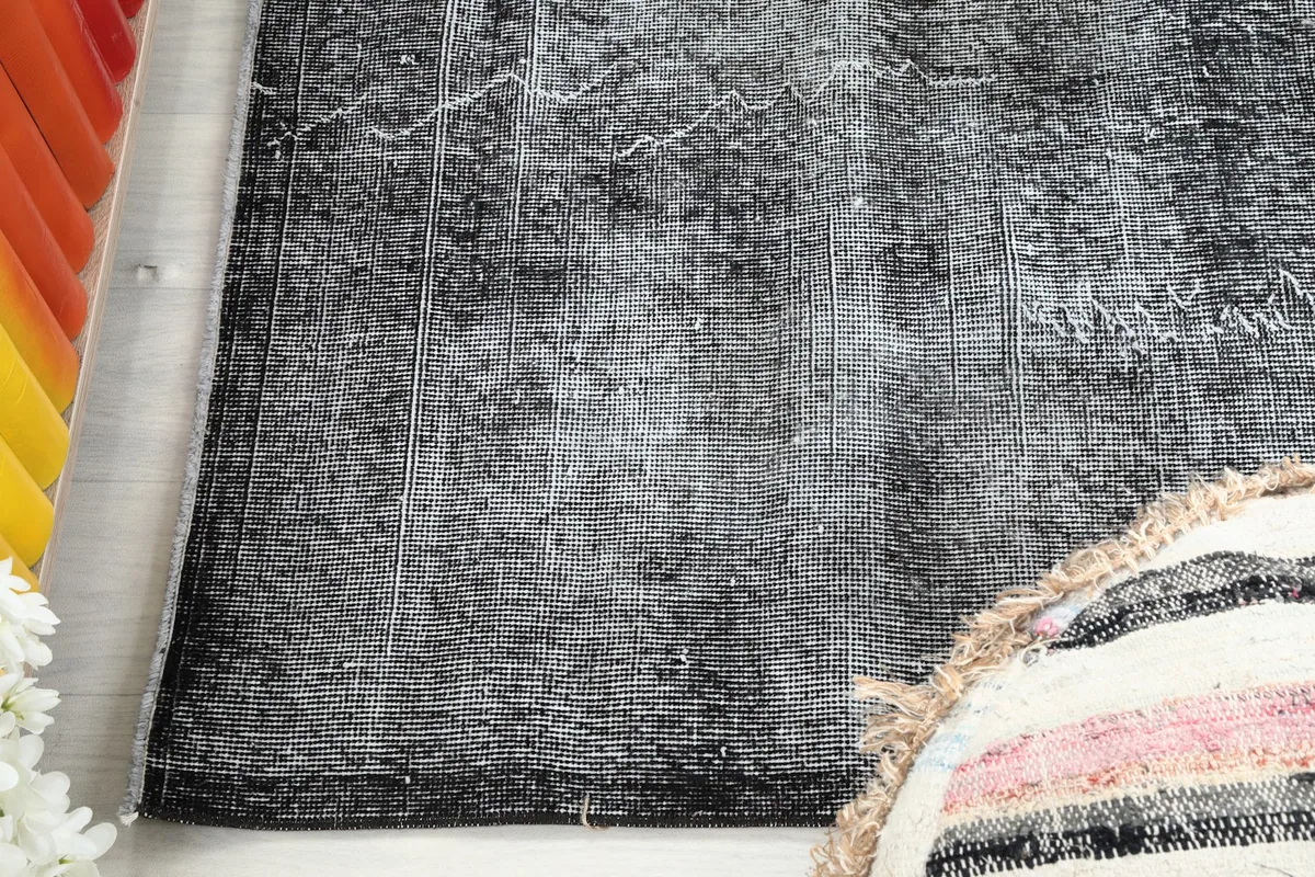 Close-up detail of the charcoal gray rug's pile and distressed areas, showing the weaving.
