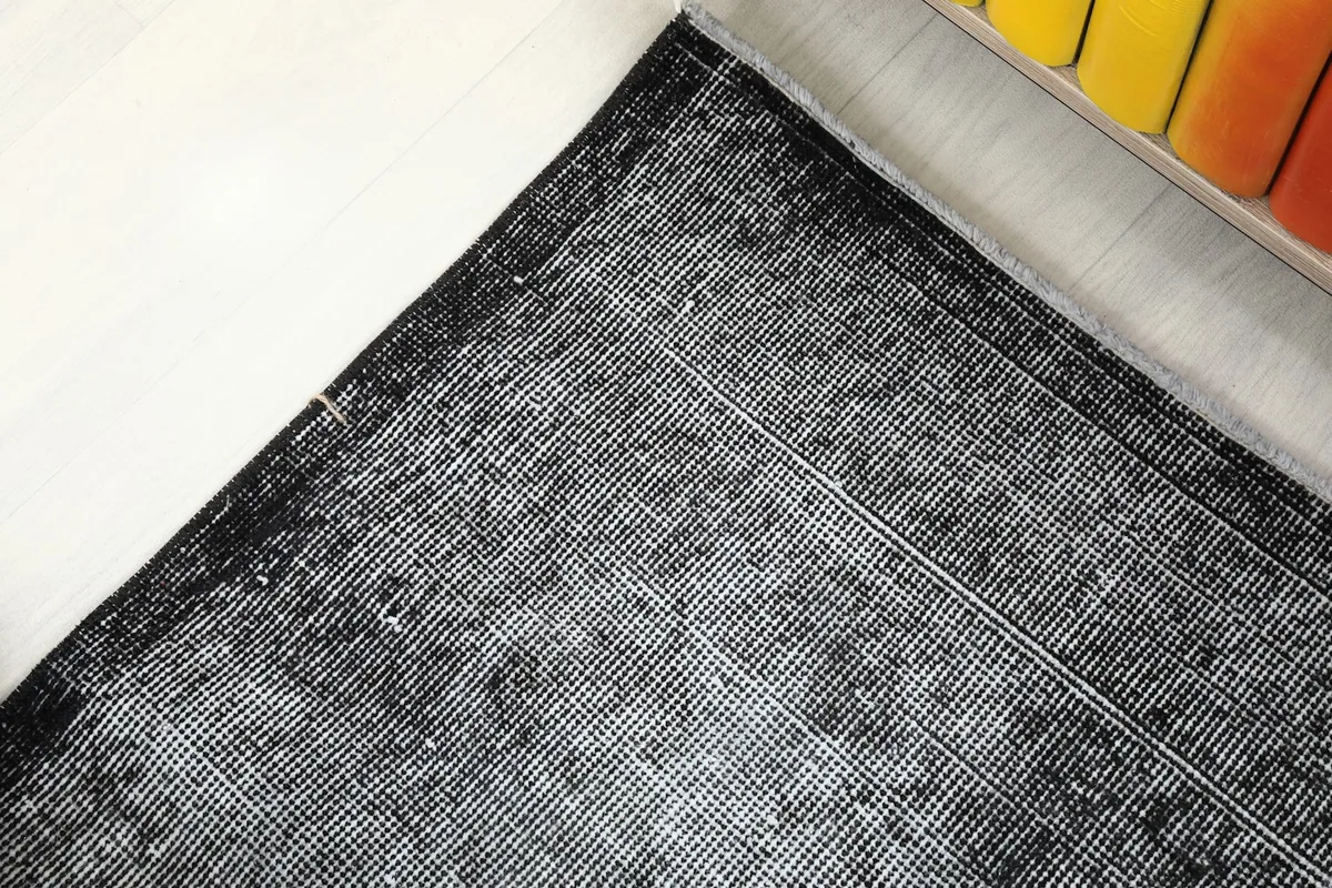 Corner detail of the charcoal gray rug, showing the edge finish and a hint of the cotton foundation.