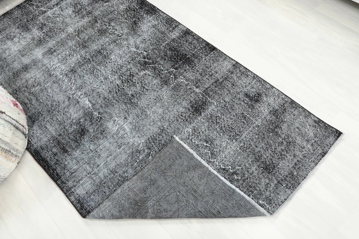 View of the charcoal gray rug with a corner folded back, revealing the reverse side and foundation.