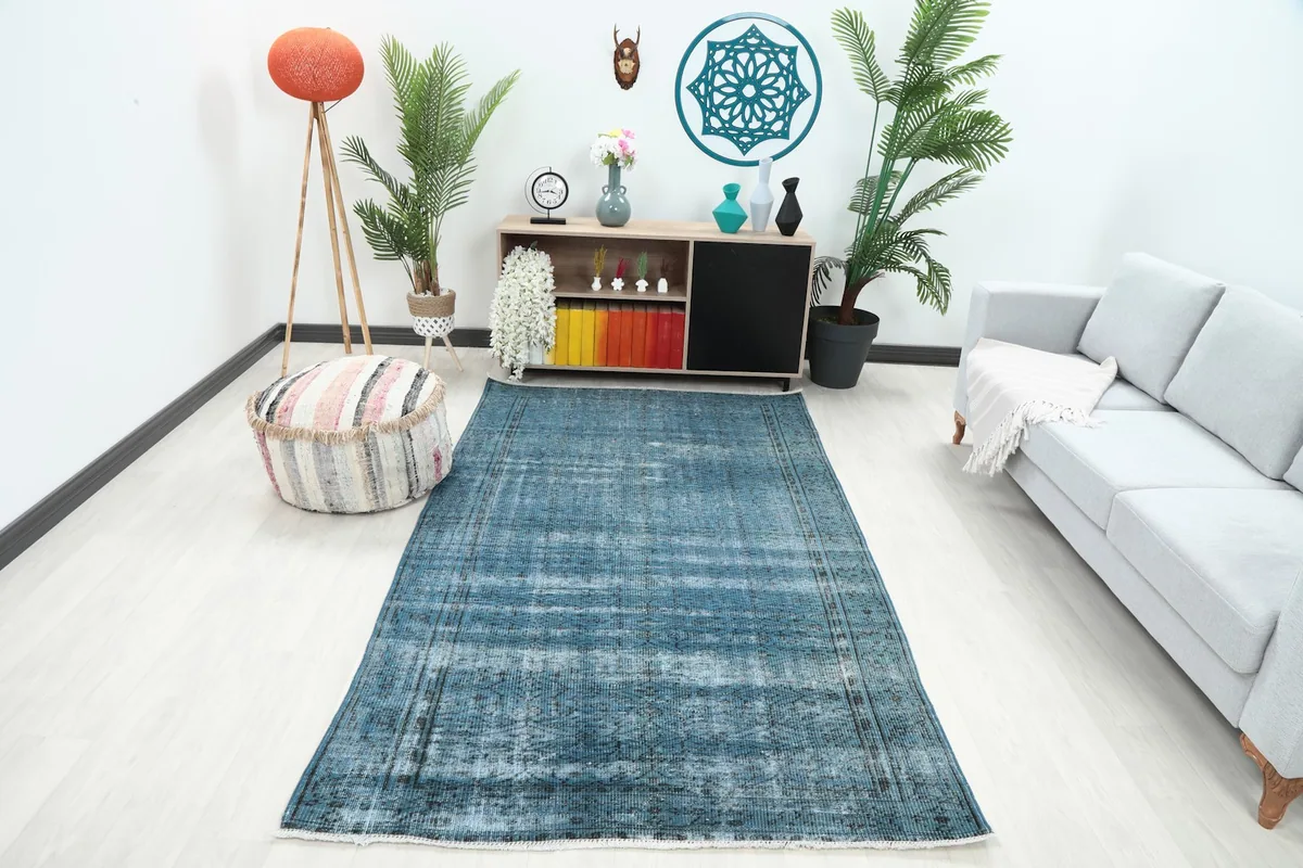 Blue distressed vintage rug placed in a modern living room setting with a light sofa and pouf.