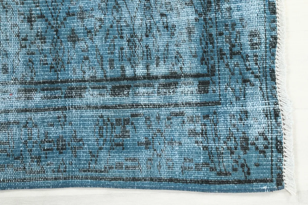 Detail view of the corner of the blue vintage rug, showing the distressed pile and subtle border design.