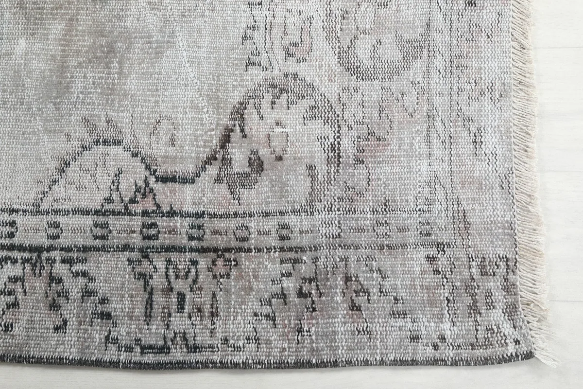 Detail of the rug's border with charcoal and beige motifs, showing the fringe