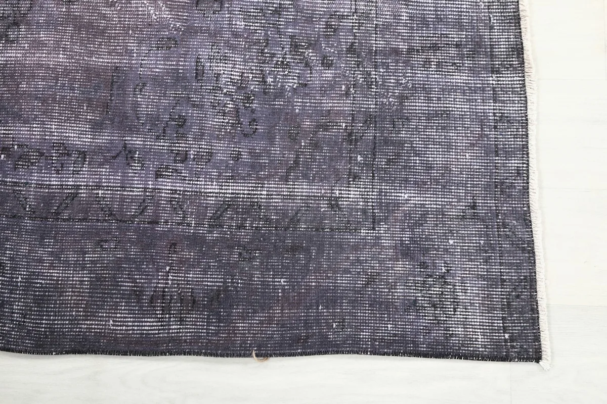 Corner detail of the purple rug, showing the blend of purple and charcoal colors and subtle wear.
