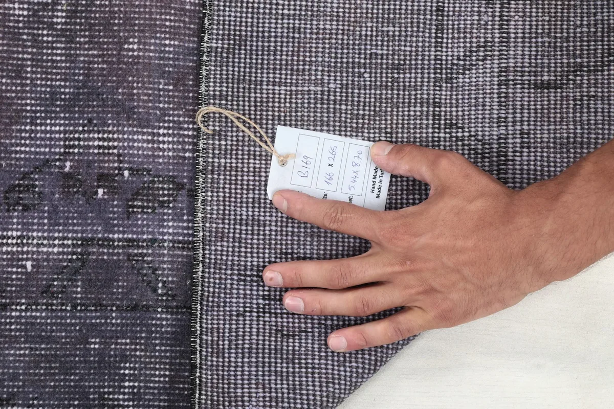 A hand holding a product tag against the back of the rug, illustrating the texture and construction.