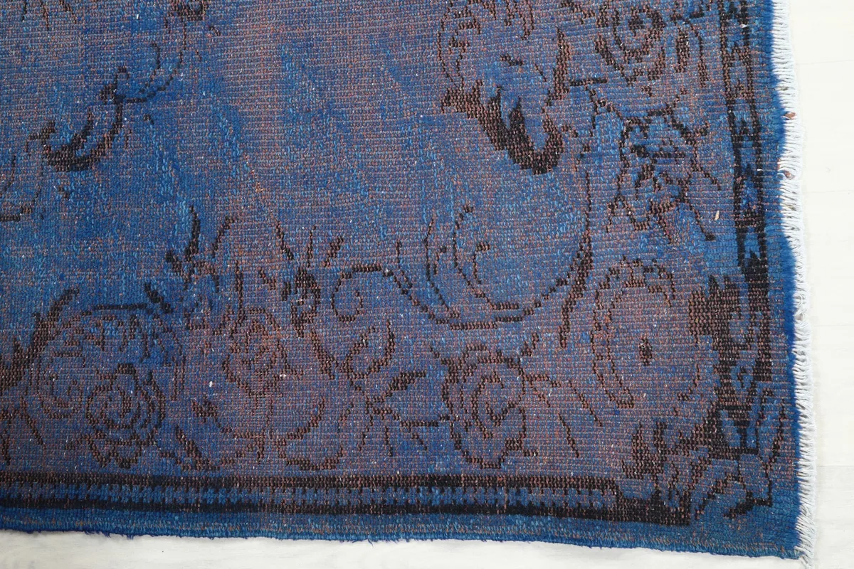 Detailed view of the corner of the blue rug, highlighting the worn floral patterns