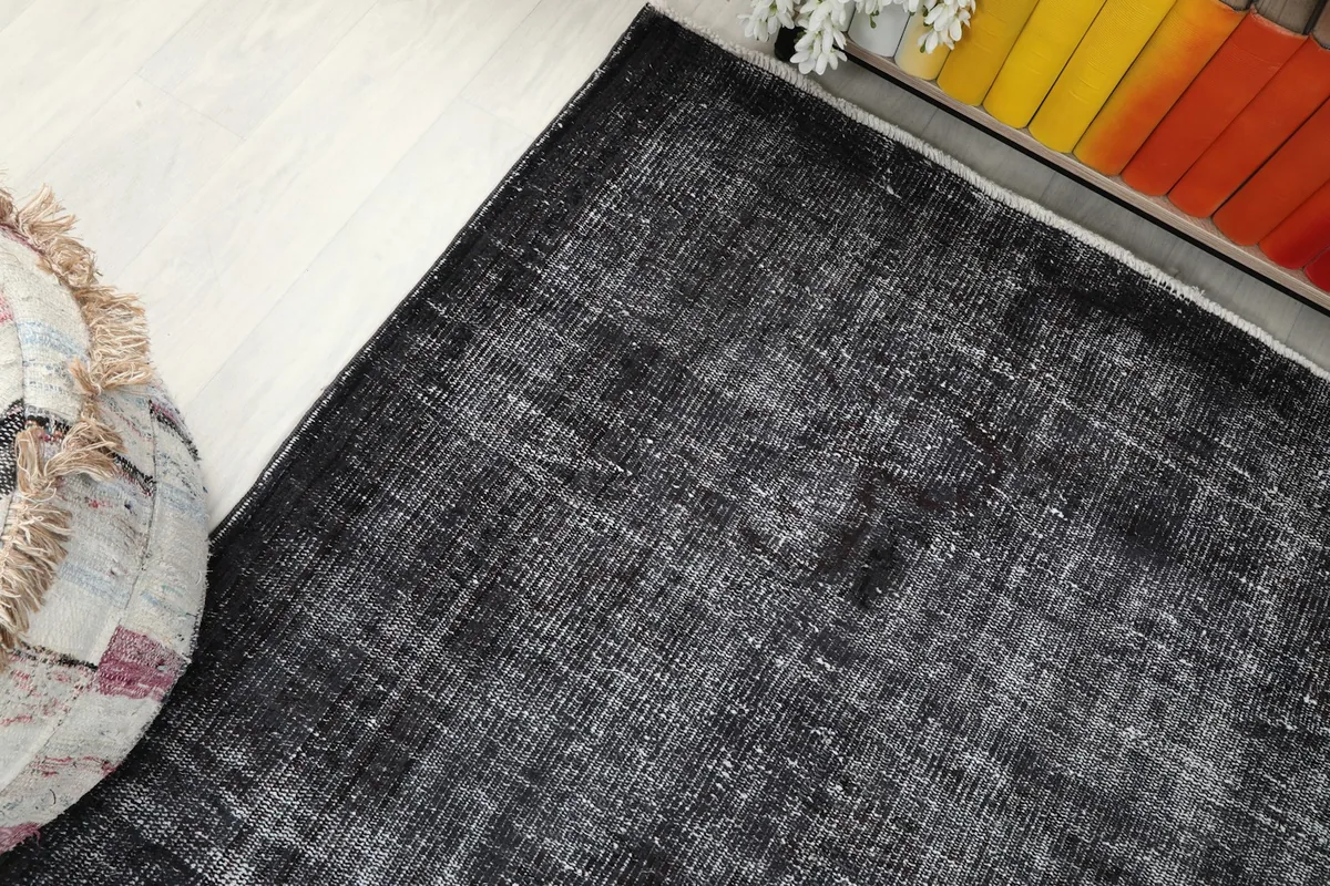 Corner view of the charcoal rug, showing its placement relative to a decorative pouf