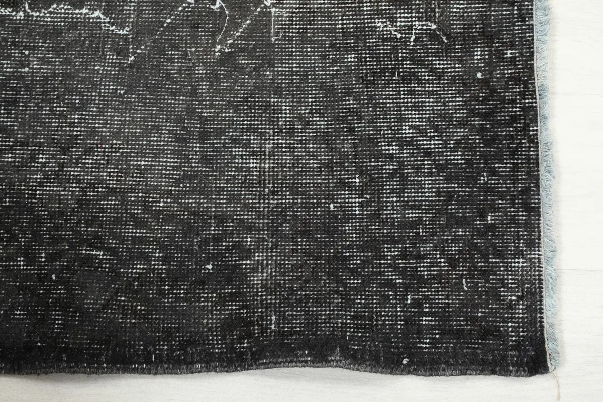Detail view of the edge of the charcoal rug, highlighting the low pile and subtle wear.