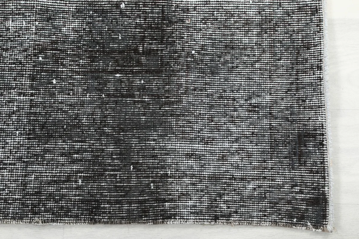 Close-up of the rug's corner, highlighting the faded charcoal and gray tones
