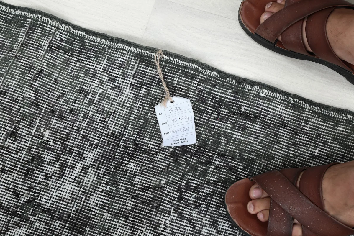 Close-up of the rug's edge with a tag, showing the detailed texture next to sandals